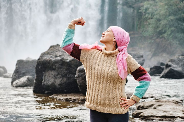 женщина в свитере и платке на фоне водопада показывает свою силу